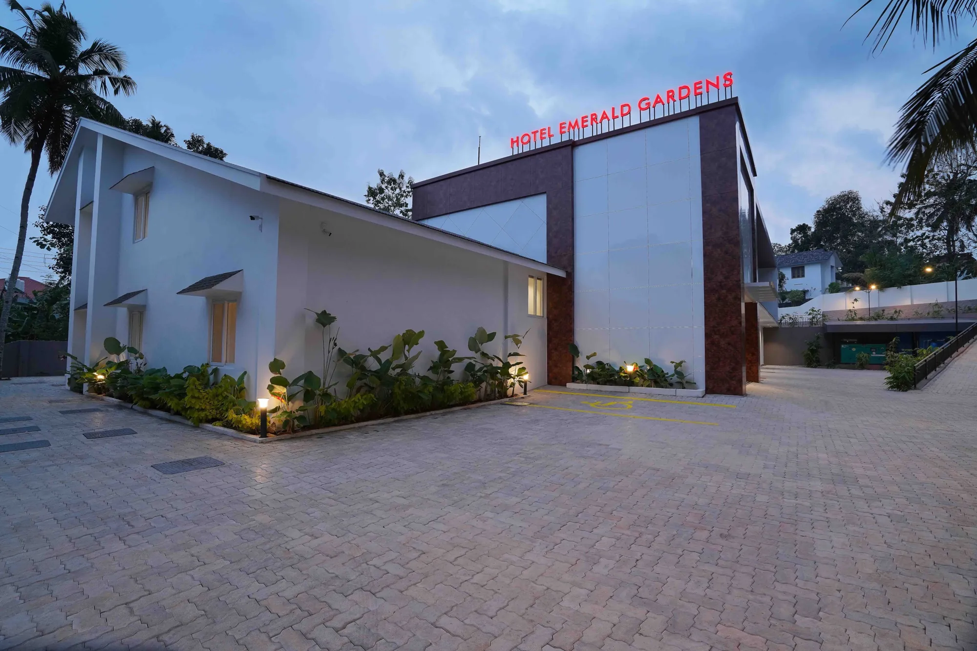 Hotel Emerald Gardens at dusk, its name lit in red above the entrance block