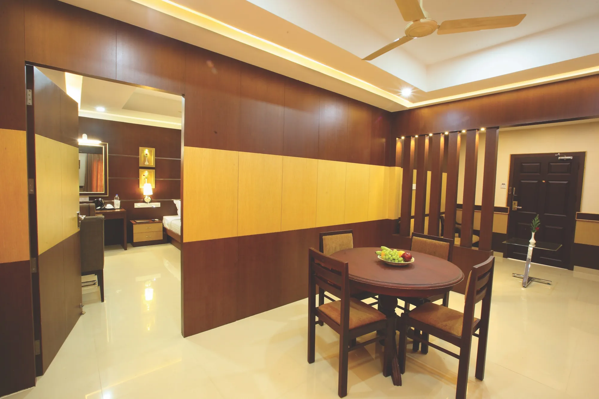 The Suite's living and dining room, with a round table for four and wood-panelled walls, opening into the bedroom